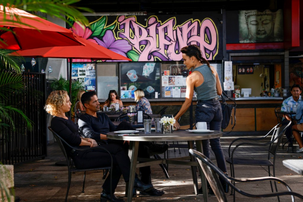 Assis à une table, Higgins (Perdita Weeks) et Magnum (Jay Hernandez) discutent avec Maya (Maya Stojan).